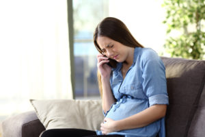 Painful pregnant woman calling doctor sitting on a couch at home