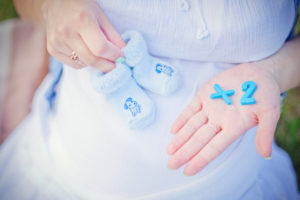 pregnant belly with woman holding baby shoes and "x2" blocks