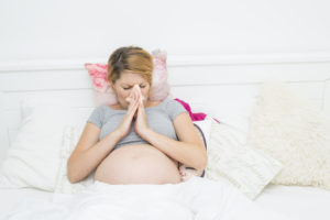 pregnant woman sneezing in bed because of allergies