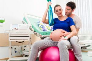 pregnant woman on exercise ball in hospital room with husband