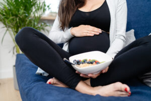 Pregnant woman with fruits oatmeal porridge sitting on bed