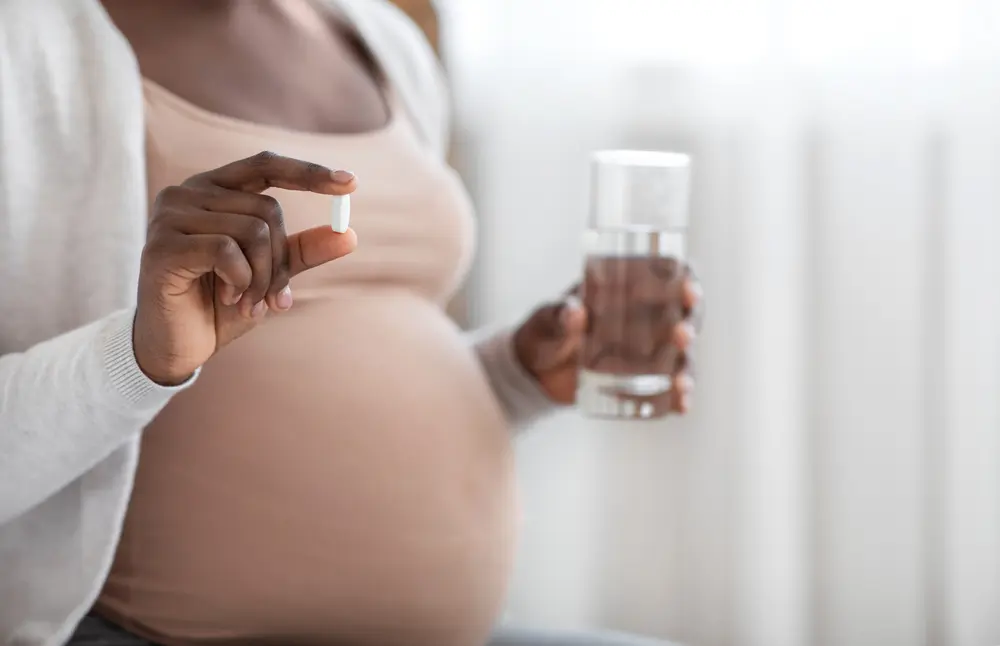 Black Expectant Lady Holding Pill In Hand And Glass Of Water